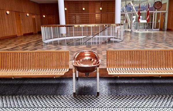 City hall entrance hall - brass drinking fountain, wooden bench, floors of different patterns,  Danish flags, top of spiral staircase leading to basement-level floor. Rådhuset, Aarhus City Hall.
