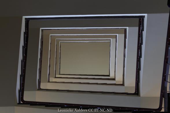 Rectangular dark lines surrounding white ceiling/plaster work coming into the middle forming the ballustrades of stairs as seen from the middle looking up.