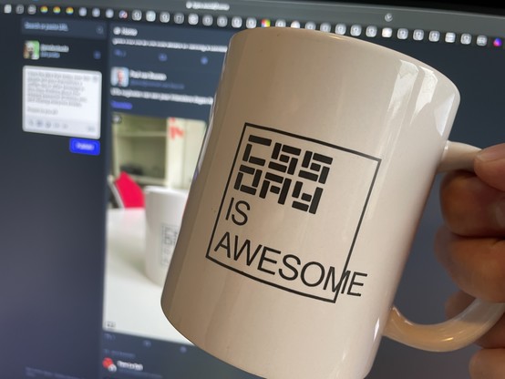 A "CSS Day is awesome" mug held up to a screen where a similar photo has been posted to a social network