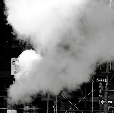 A black and white street photograph capturing a large plume of steam rising vertically and billowing outwards. The steam dominates the center and upper portion of the frame, creating a soft, ethereal texture against the dark, gritty background. The origin of the steam is low in the frame, a utility vent, and is partially obscured by the framing of the image. The background consists of dark, silhouetted building facades and silver construction scaffolding. Several street signs are visible on the right, including a sign reading "Church St" and a sign below it with a white arrow indicating "ONE WAY." A partial, lighter-colored sign is partially visible with obscured writing through the steam on the left. The scene is high contrast, and the overall mood is dramatic and characteristic of an urban environment, emphasizing texture and the stark contrast between light and shadow.