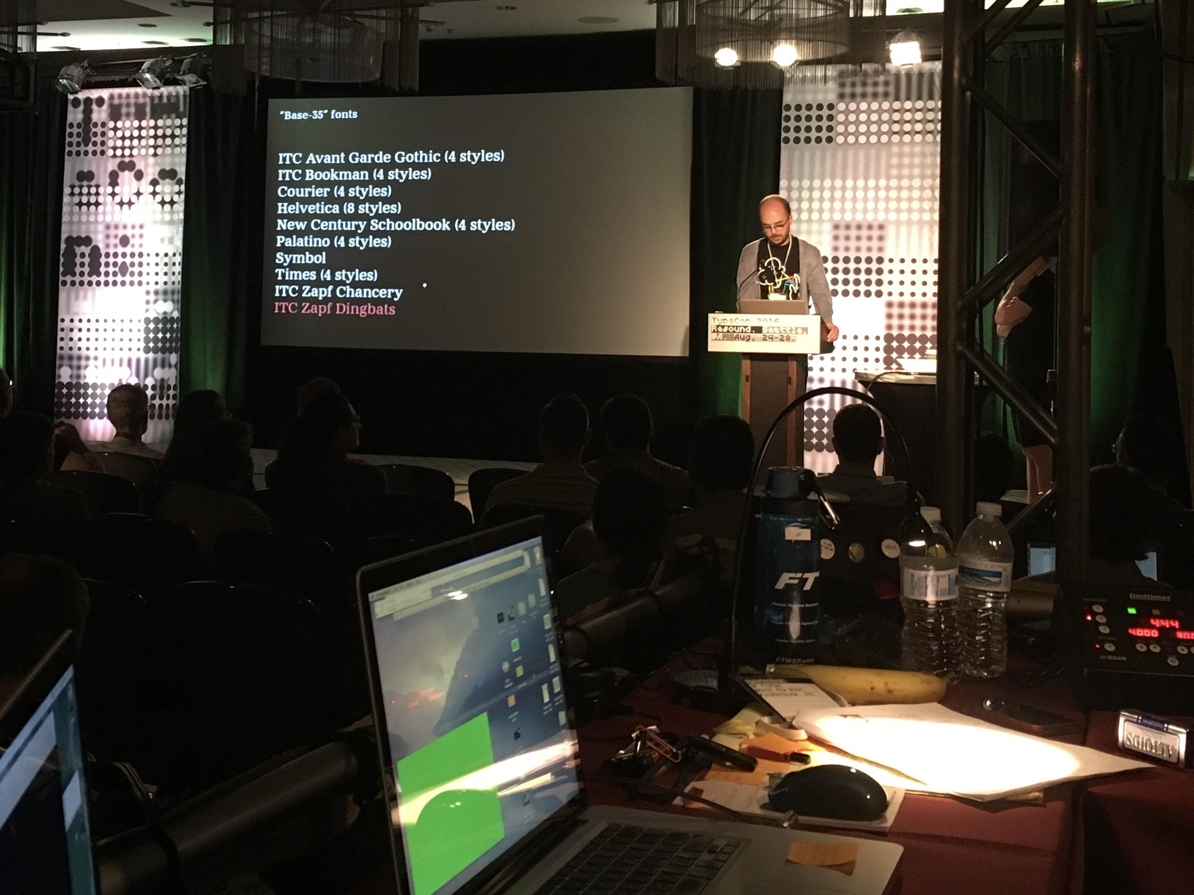 Photo of a ballroom with a person presenting at the front behind a podium. On the screen:
“Base-35” Fonts:
ITC Avant Garde Gothic (4 styles)
Helvetica (8 styles)
New Century Schoolbook (4 styles)
Palatino (4 styles)
Symbol
ITC Zapf Chancery
ITC Zapf Dingbats