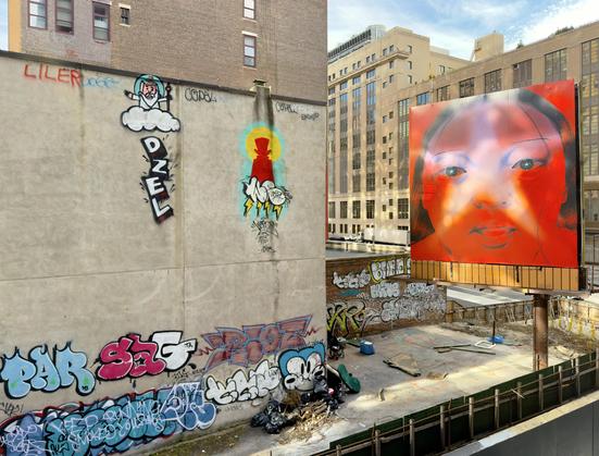 A color, medium-angle photograph captures the street art scene from the High Line in Manhattan. The focal point on the left is a large, unadorned concrete wall covered in several distinct styles of graffiti. Prominently featured are two figurative pieces: a cartoon-style figure of an old man with a beard sitting on a cloud (God) and below it, a silhouette of a top-hatted figure in red and black, both surrounded by bright yellow and blue halo effects and lightning bolts. The lower part of the wall and surrounding brick structures are heavily tagged with bubble letters and complex throw-ups in various colors like red, blue, and black. Debris and scattered construction materials are visible in the fenced-off lot below. Dominating the right side of the image is a massive, brightly colored billboard-style artwork featuring a close-up, stylized portrait of a woman's face, primarily rendered in a vibrant red and orange palette with a translucent star shape quality over her eyes. This large, contemporary piece stands elevated on poles above the street. The afternoon sky is partly cloudy, with strong natural light illuminating the scene.