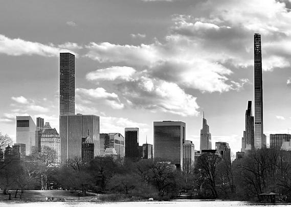 A noir, wide-angle photograph in landscape orientation that captures the Manhattan skyline as seen from Central Park during the winter. In the foreground, a dark, calm body of water reflects a hint of the sky, bordered by a shoreline where several small figures of people are walking. The middle ground is filled with a dense thicket of bare, leafless deciduous trees, their intricate dark branches creating a stark contrast against the buildings. A small wooden gazebo sits nestled among the trees on the far right bank, adding a quiet, scenic element to the park landscape. The background is dominated by a row of towering skyscrapers under a bright sky filled with voluminous, textured clouds. Two exceptionally thin "pencil towers" bookend the composition: 432 Park Avenue on the left with its distinct grid-like facade, and 111 West 57th Street on the right, tapering sharply toward the top. Between them, a mix of modern glass towers and classic architectural styles, including the slanted roof of the Citigroup Center, creates a jagged and iconic horizon line. The lack of color emphasizes the dramatic lighting, casting deep shadows across the park and highlighting the reflective surfaces of the urban architecture.