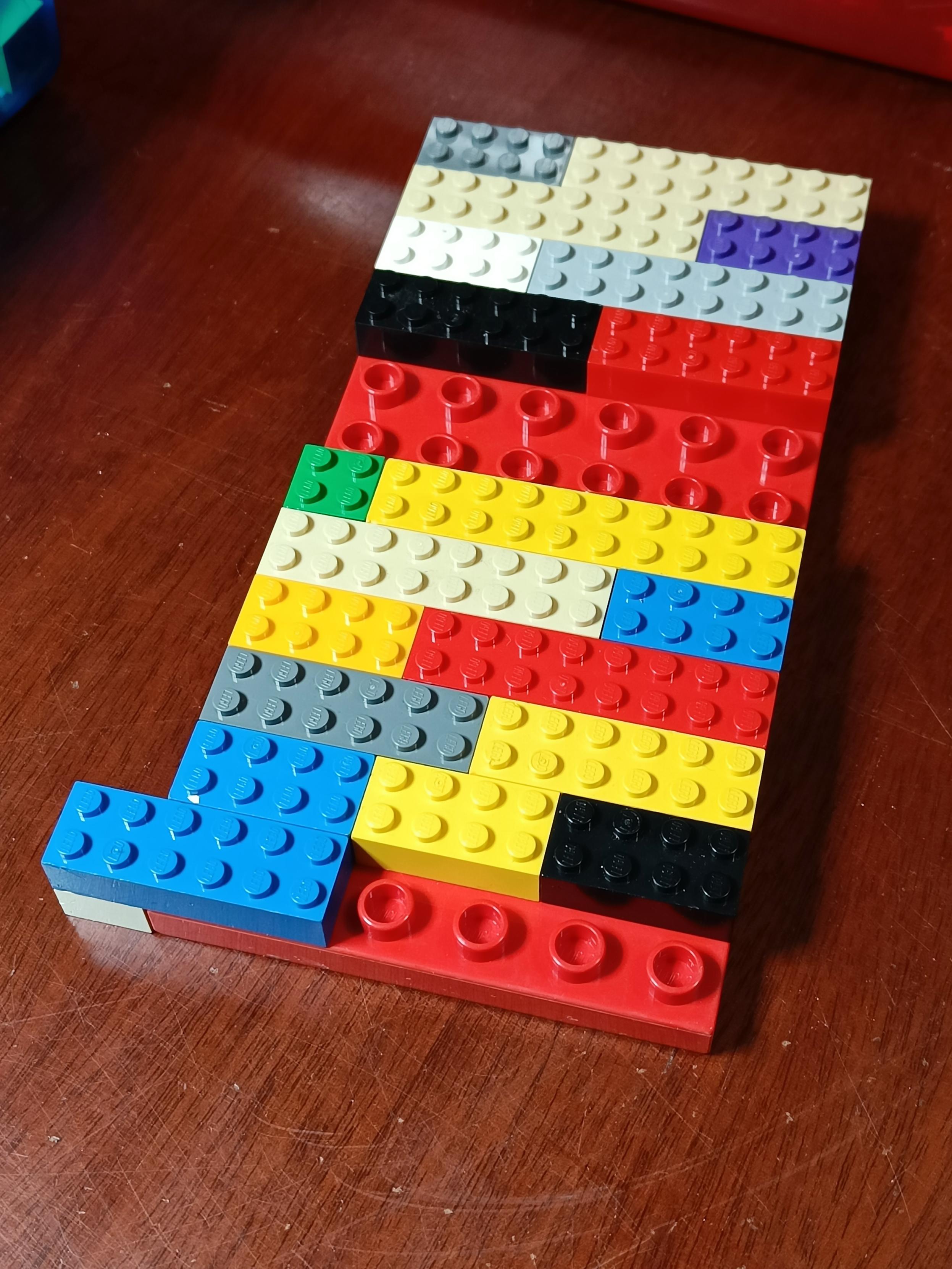 A colourful but simple Lego arrangement. Mostly made of regular basic Lego bricks of various colours. They are laid in a single layer on top of a Duplo baseplate which has studs 2x the size of Lego studs. In a couple of places gaps let you see the Duplo board underneath. On one corner I've overlapped a regular Lego brick to show that the thickness between Duplo and Lego matches.