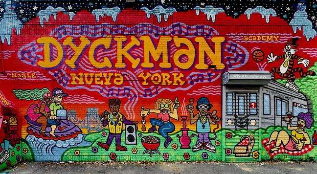 A color, wide-angle photograph in landscape orientation that captures a vibrant, sprawling mural that spans a brick wall, featuring the bold, stylized text "DYCKMAN NUEVA YORK", “NAGLE” and “ACADEMY” in yellow and orange. The artwork is framed by a wintery top border of blue icicles and white snowflakes against a dark sky. In the center, cartoonish, expressive characters celebrate local culture: a man and woman on a jet ski riding a wave, another performs with a microphone and large speaker, a woman grills food while holding a green bottle, and a man holds a chicken drumstick near a pink hookah. On the far right, a woman relaxes on a picnic blanket near a painted silver subway train labeled "1 UPTOWN," while a tiger character in a gold chain leaps through the air above her. The mural uses a saturated palette of primary reds, greens, and purples, tied together by swirling purple musical notes that drift across the entire composition. Local landmarks, like the George Washington Bridge, appear in the background behind the figures. The style is reminiscent of classic graffiti and street-style illustration, with thick black outlines and high-contrast colors. Small details in include scattered flowers on the green grass at the base and various artist tags, including "@THESNOEMAN" on a grey storefront awning. The scene is evenly lit by partly overcast morning sunlight, and the grey concrete sidewalk is partly visible beneath the mural.