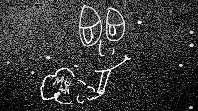 A noir, high-contrast photograph in landscape orientation that captures a simple, hand-drawn graffiti doodle in white ink on a dark, textured bathroom stall door inside of a bar on the Upper West Side of Manhattan. The drawing features a whimsical face with large, droopy, oval-shaped eyes and heavy eyelids that give it a dazed expression. A long, thin nose sits above a wide, lopsided grin, from which a cannabis joint protrudes. A small, stylized puff of smoke exhales from the end of the blunt, forming a cloud that contains the word "MOTH" written in capital letters. The background is a rough, granular material dotted with small white specks resembling stars.
