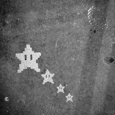 A noir, medium-angle photograph in square aspect ratio taken along 42nd Street at the intersection with Ninth Avenue in the Hell’s Kitchen neighborhood of Manhattan that captures a gritty section of a sidewalk from an overhead perspective. The asphalt is weathered and textured, speckled with dark pits and light-colored debris. In the upper-right corner, a faint footprint made with paint from a sneaker is visible. The lighting is harsh and dramatic, creating deep shadows and bright highlights that emphasize the rough, industrial character of the pavement. Four pixelated Super Mario "Power Stars" have been stenciled onto the ground in white paint, appearing to trail upward from the bottom center toward the middle left. The stars decrease in size as they descend the line, with the largest star at the top being the most prominent. The stars feature the iconic two vertical black lines for eyes, rendered in a 16-bit aesthetic that contrasts sharply with the organic, messy texture of the street.