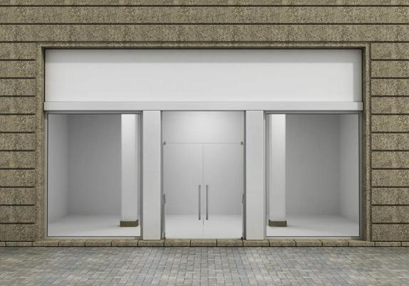 A color, wide-angle photograph of a small pure white storefront with empty floors and walls.