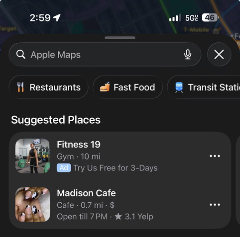 A cropped screenshot of Apple Maps on iOS 26.6.1 displaying two suggested places beneath the search field. The first, for ‘Fitness 19’ is labeled as an ad, the second, for ‘Madison Cafe’ is just recommended based on user interest.