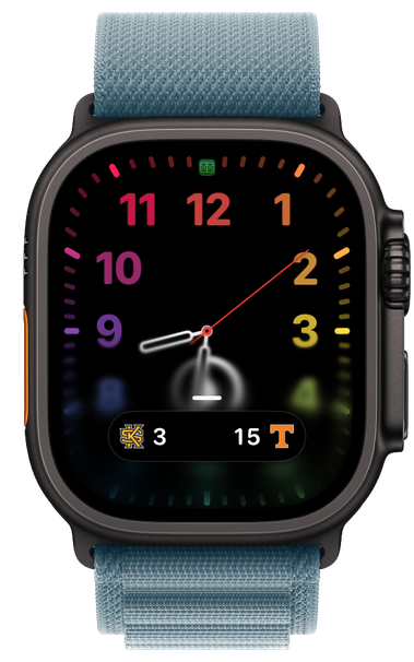 A framed watchOS 27 screenshot showing a live activity pill overlayed at the bottom of a rainbow colored analog watch face. Showing a current college football sport score of 3 Kennesaw State vs 15 Tennessee 