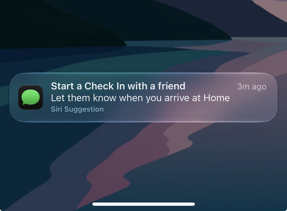A cropped screenshot of the lock screen on iOS 27 showing a notification from the Messages app: Start a Check In with a friend Let them know when you arrive at Home Siri Suggestion